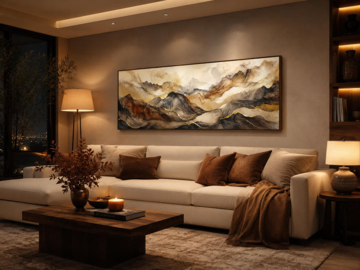 Long horizontal abstract mountain wall art in earthy brown and gold tones above a white sofa.
