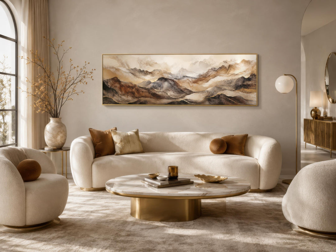 Long horizontal abstract mountain wall art in earthy brown and gold tones above a white sofa.