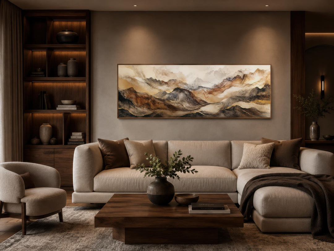 Long horizontal canvas art featuring abstract mountains in earthy brown and gold tones above a sofa.