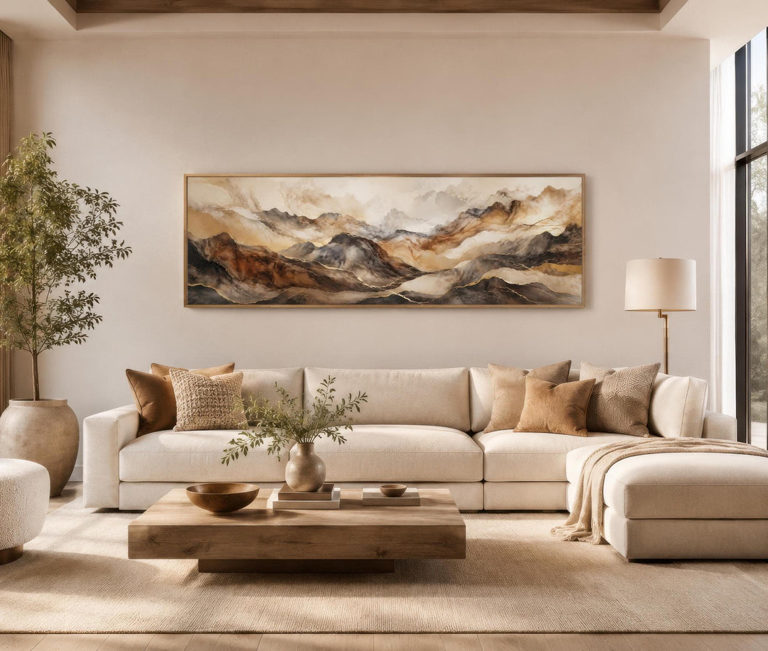 Long horizontal canvas art featuring abstract earthy brown and gold mountain layers above a sofa.