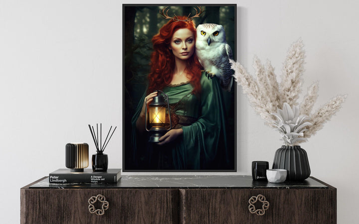 Framed canvas art of an antlered woman with red hair and a white owl, holding a glowing lantern.