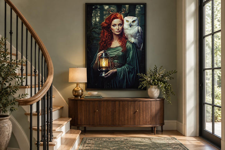 Framed canvas art of Elen of the Ways goddess with an owl and lantern above a wooden sideboard.