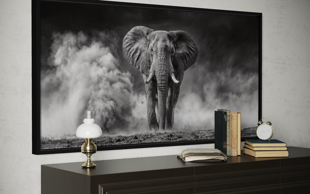 Framed black and white canvas print of an elephant in a dust cloud, styled on a dark wood dresser.