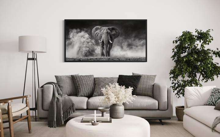 A framed black and white canvas print of an elephant in dust hangs above a modern living room sofa.