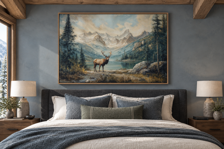 Antique framed canvas wall art of an elk by a lake in a mountain landscape above a bedroom headboard.