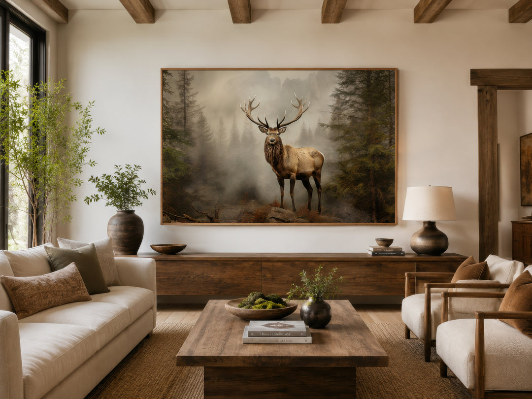 Framed elk painting in a misty fir forest, displayed above a wooden console in a rustic living room.