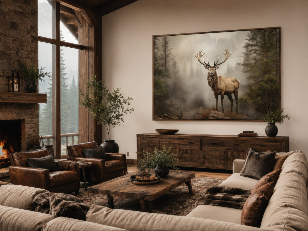 Elk in a misty fir tree forest painting framed above a wooden sideboard in a rustic living room.
