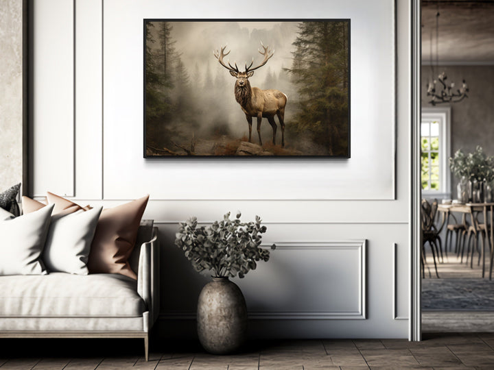 Framed elk painting in a misty fir forest, hung above a sofa in a rustic living room.