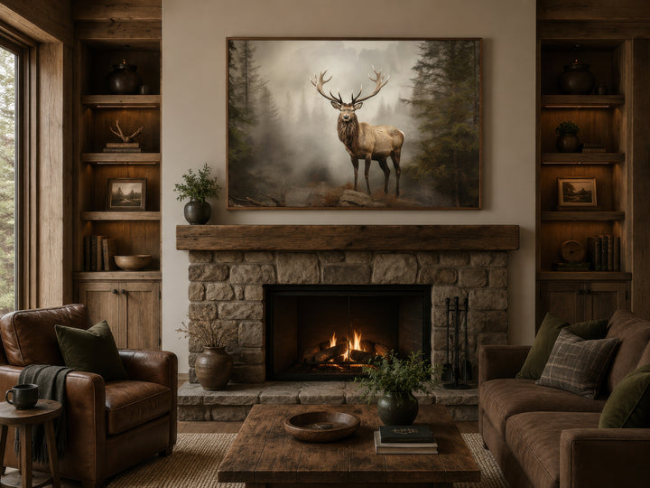 Elk painting in a misty fir forest, framed above a stone fireplace in a rustic cabin living room.