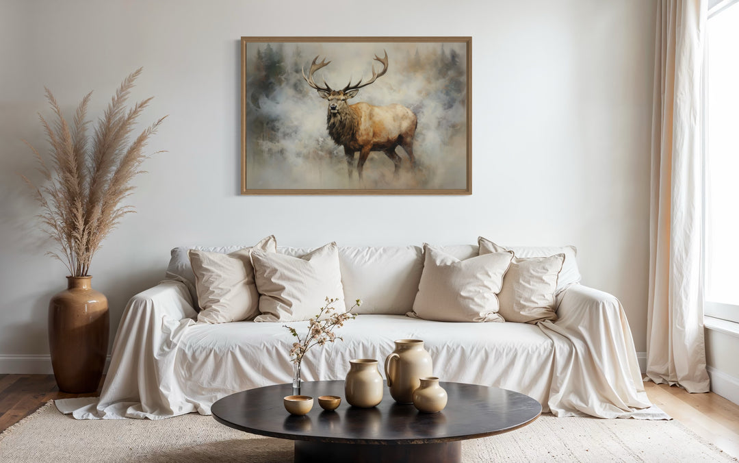 Framed canvas wall art of a majestic elk in a smoky forest above a white sofa in a rustic room.