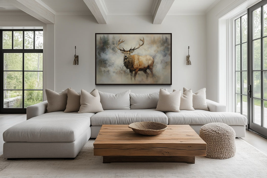Elk in smokey forest canvas wall art hanging above a light gray sectional sofa in a living room.