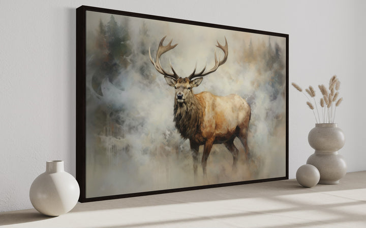 Framed canvas wall art of a majestic elk in a misty, smoky forest with neutral vases on a shelf.
