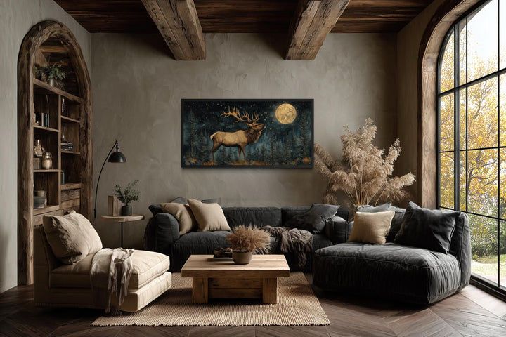 Horizontal wall art of an elk in a moonlit forest hanging in a rustic lodge-style living room.