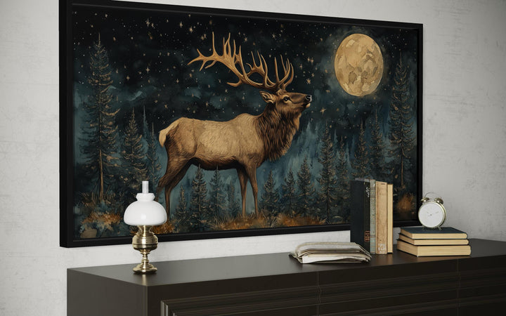 Framed wall art of a majestic elk in a moonlit forest, displayed above a dark wood console.
