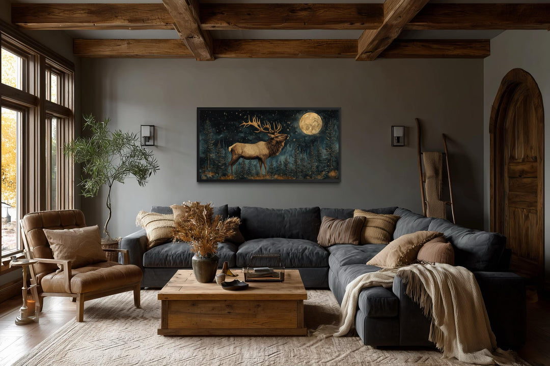 Horizontal wall art of an elk in a moonlit forest hanging in a rustic lodge-style living room.