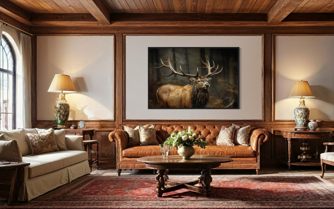 Framed canvas wall art of a majestic elk with large antlers in a dark forest above a leather sofa.