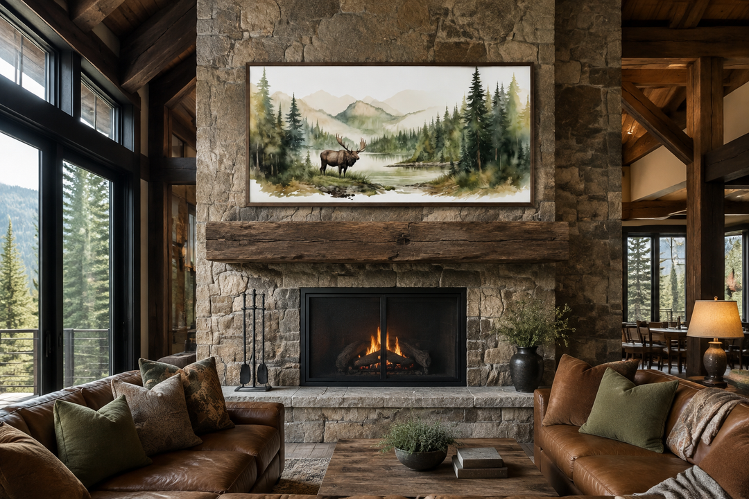 Framed watercolor canvas print of an elk in a mountain forest above a rustic stone fireplace.