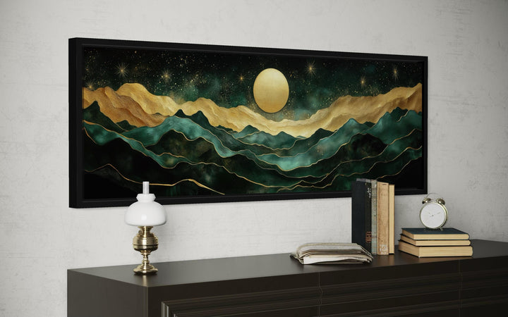 Panoramic wall art of emerald green and gold mountains under a glowing moon in a black frame.