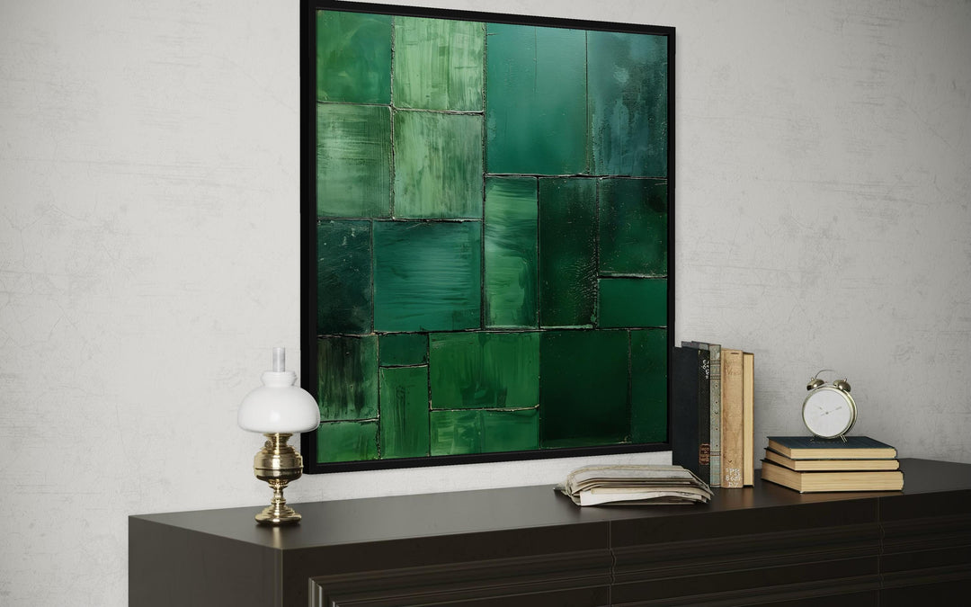 Modern geometric emerald green abstract painting on a square canvas displayed above a dark console.