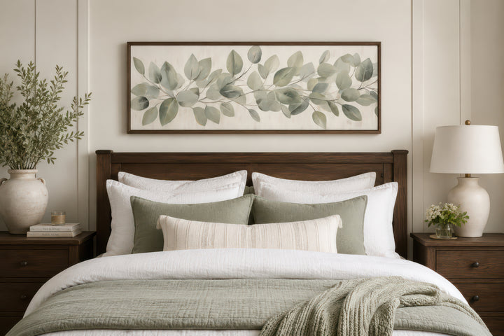 Eucalyptus leaves painted on a long horizontal framed canvas wall art above a bed.