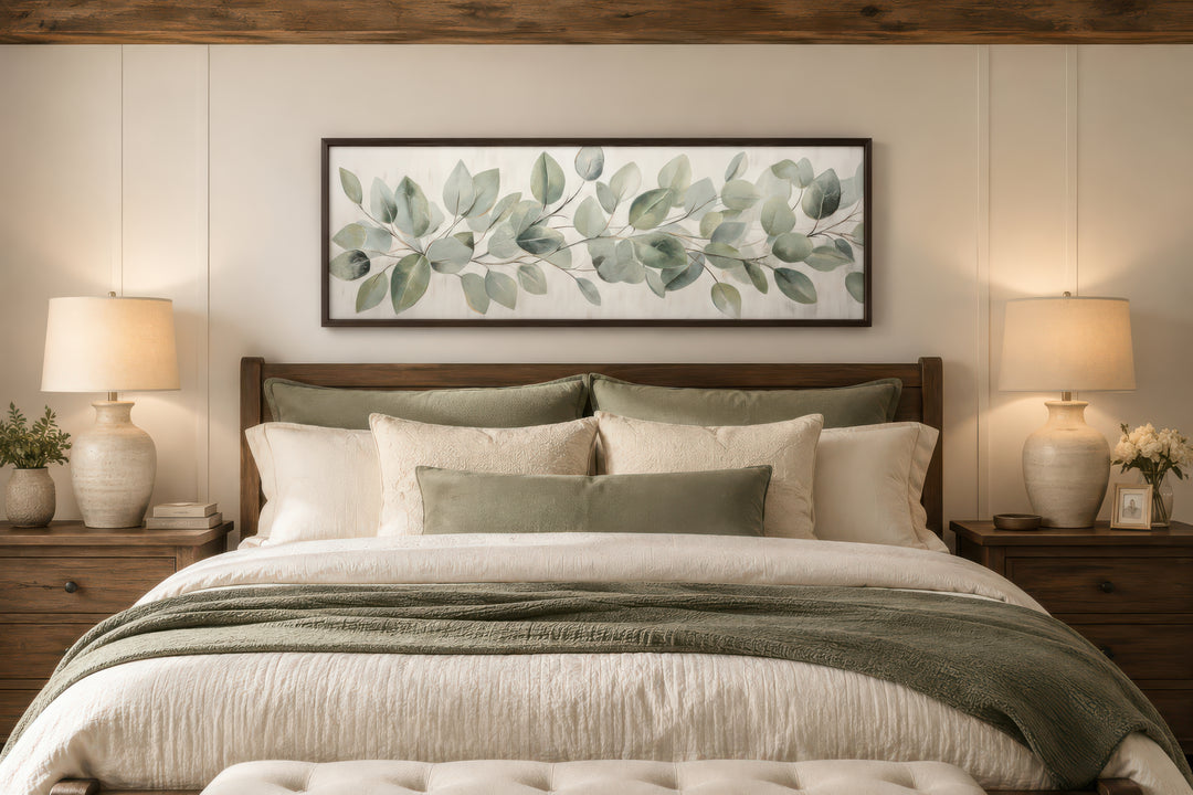 Long horizontal framed canvas wall art featuring painted eucalyptus leaves above a bed.
