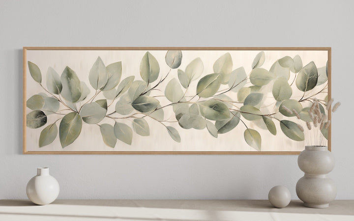 Long horizontal framed canvas wall art featuring painted eucalyptus leaves on a rustic background.