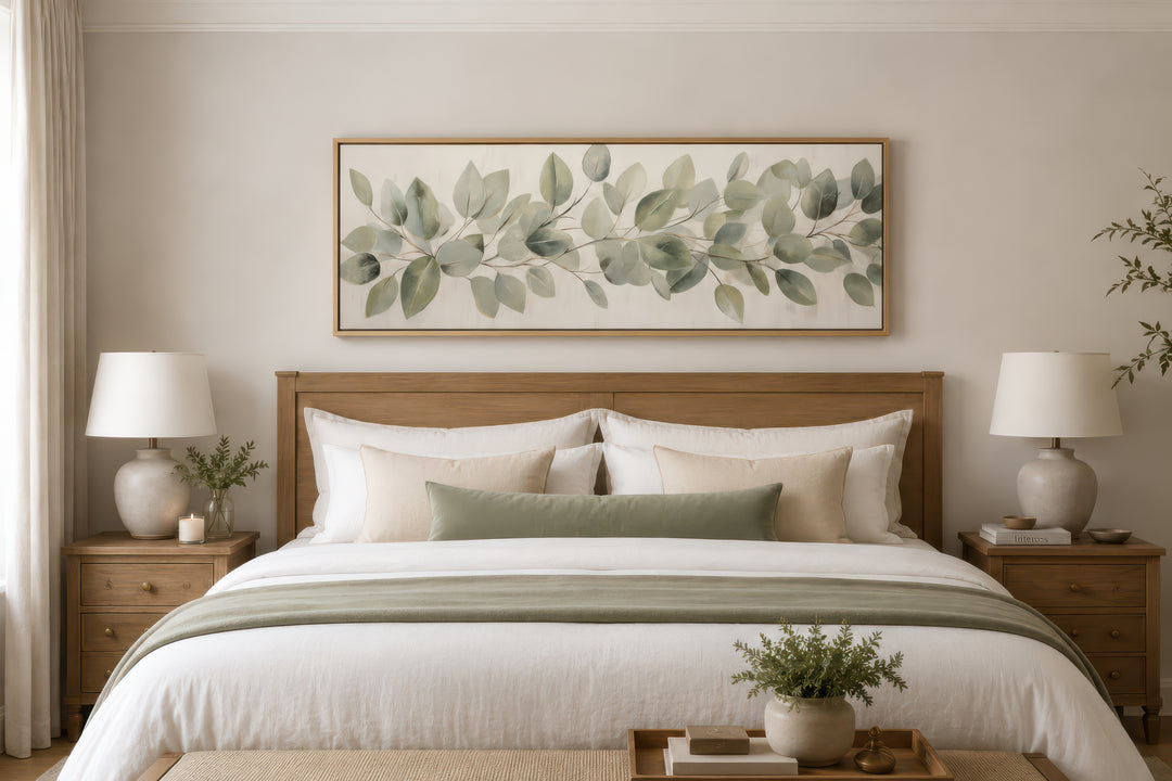 Horizontal framed canvas wall art featuring painted eucalyptus leaves above a wooden bed frame.