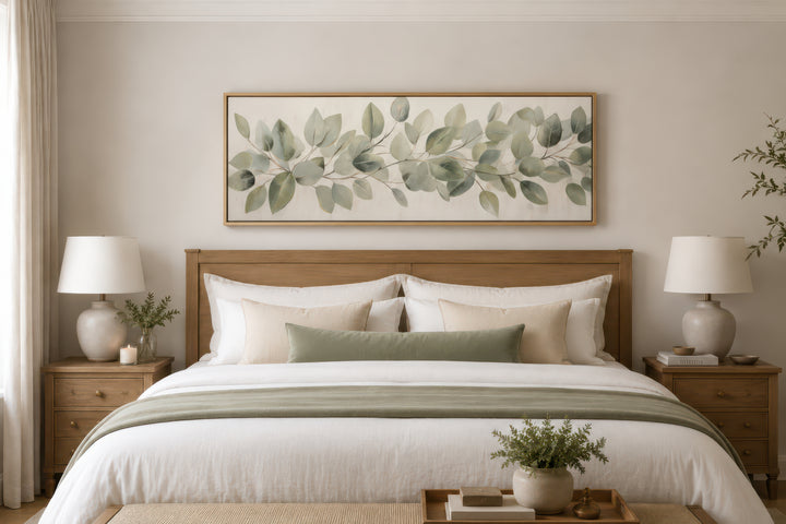 Horizontal framed canvas wall art featuring painted eucalyptus leaves above a wooden bed frame.