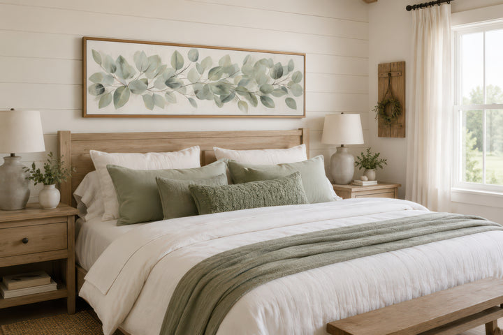 Long horizontal framed canvas wall art featuring painted eucalyptus leaves above a farmhouse bed.
