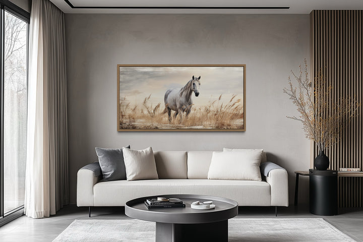 Farmhouse framed canvas wall art of a white horse in a golden wheat field above a modern sofa.