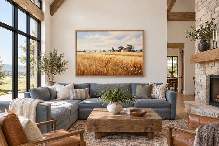 Rustic wheat field landscape painting in a wood frame above a blue sectional sofa.