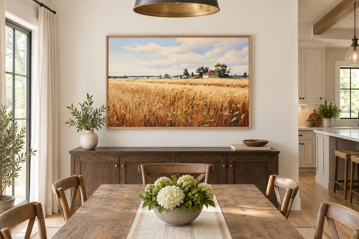 Rustic wheat field landscape painting in a wooden frame above a dark wood sideboard in a dining room.
