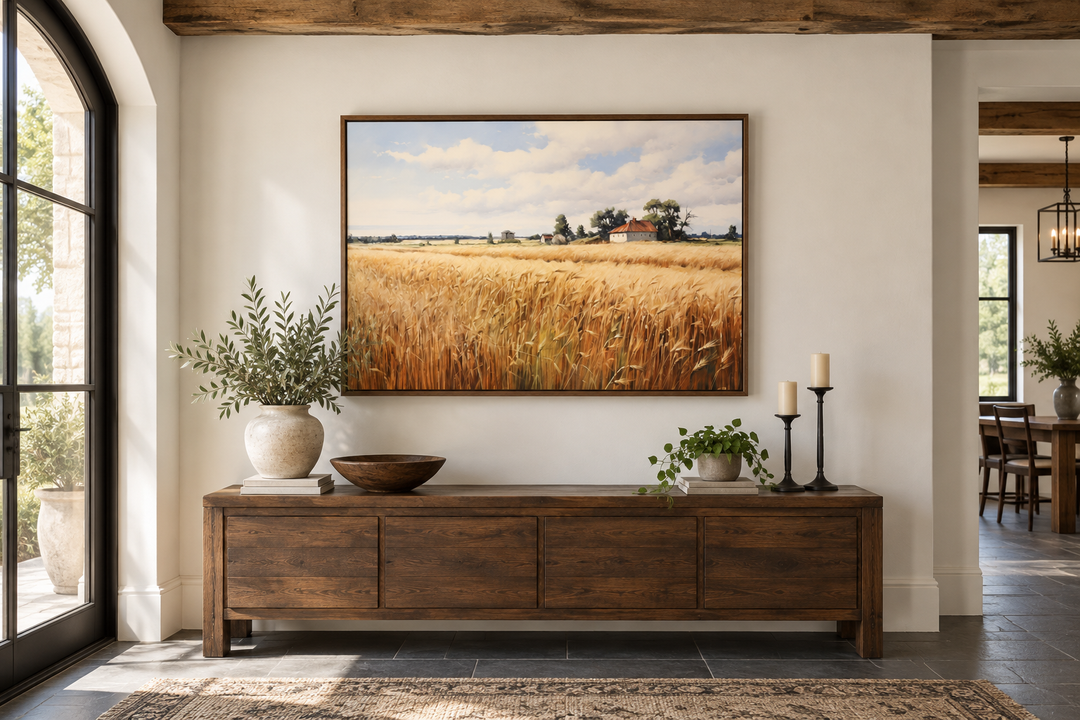 Rustic wheat field landscape painting in a wood frame above a dark wood sideboard.