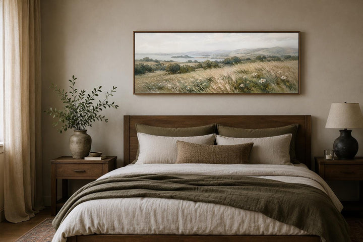 Long horizontal canvas art of a neutral farmhouse grass field landscape above a wooden bed frame.