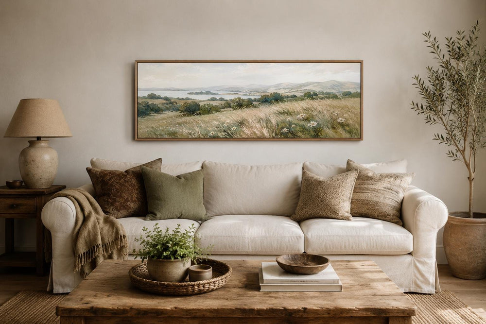 Long horizontal canvas art of a farmhouse grass field landscape above a neutral sofa.