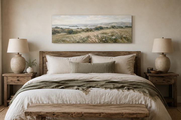 Long horizontal canvas art of a neutral farmhouse grass field landscape above a wooden bed frame.