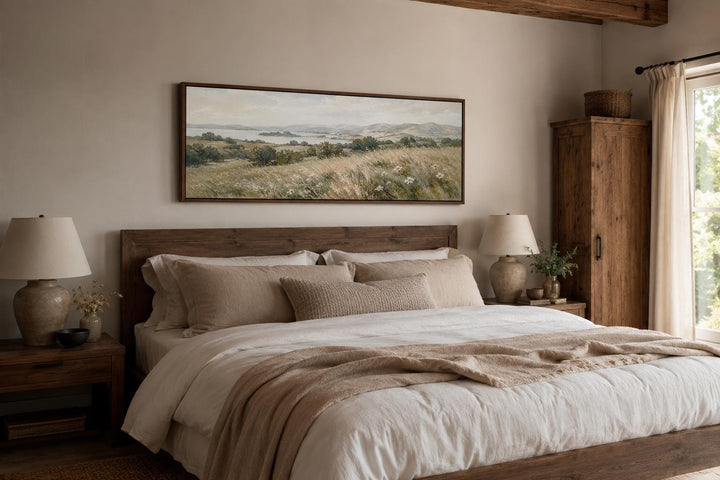 Long horizontal canvas art of a neutral grass field landscape hanging above a wooden bed frame.
