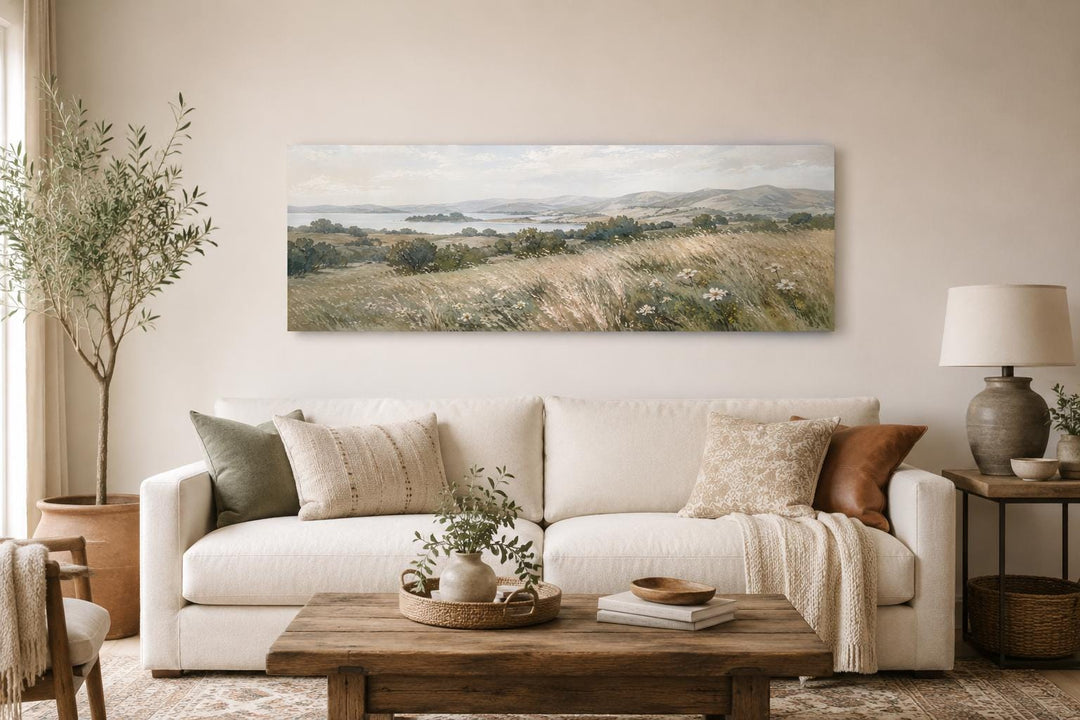 Long horizontal canvas art of a neutral farmhouse grass field landscape above a white sofa.