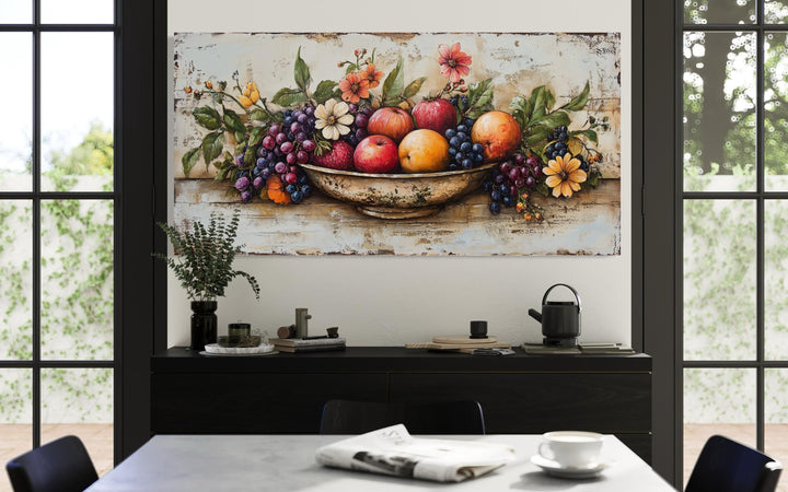 Rustic fruit bowl painting on wood canvas print hanging above a black sideboard in a dining room.
