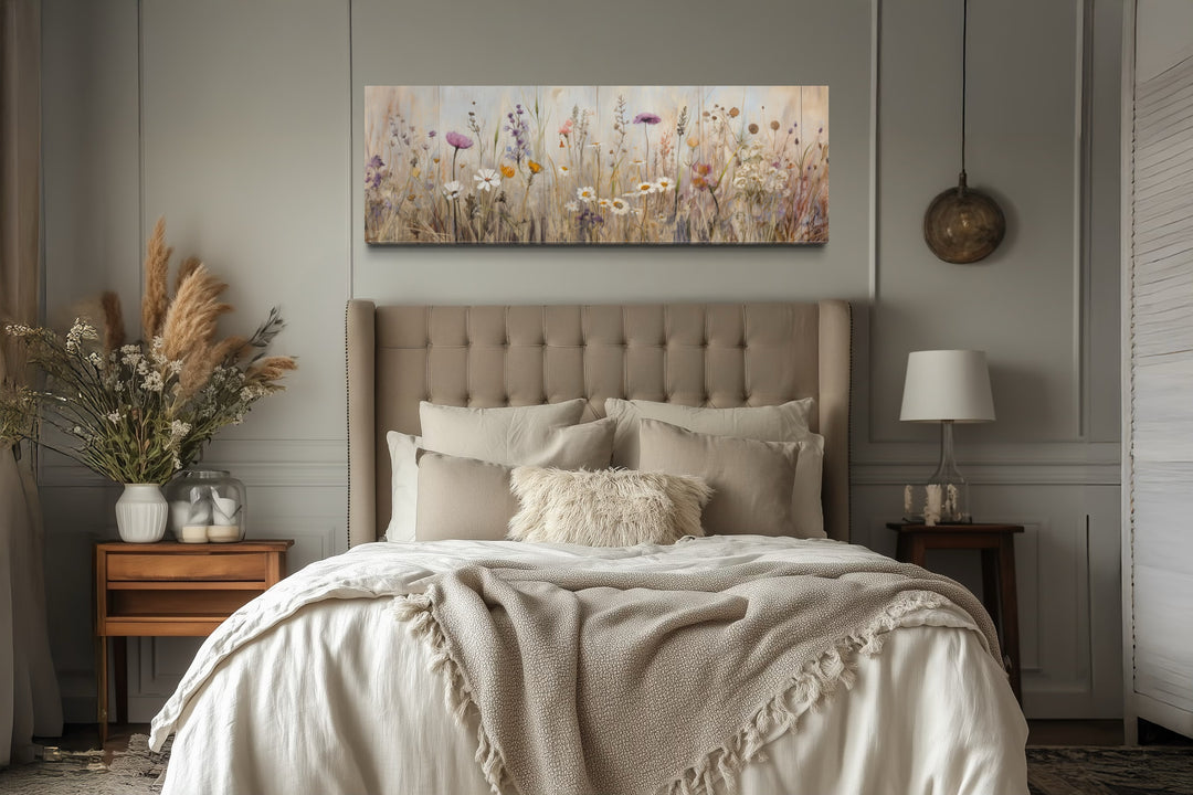 Horizontal framed canvas wall art of a neutral wildflower field above a tufted bed headboard.