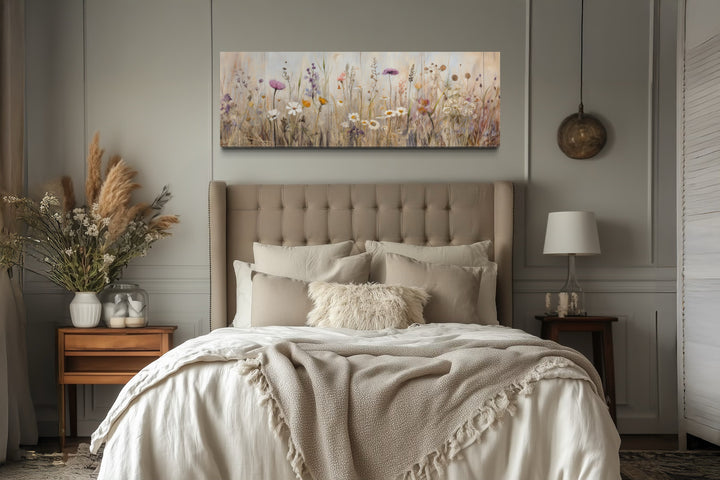 Horizontal framed canvas wall art of a neutral wildflower field above a tufted bed headboard.