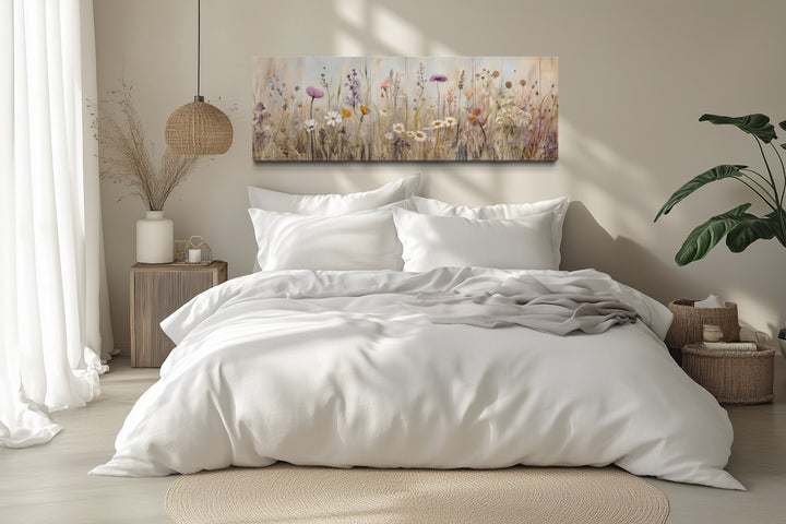 Horizontal framed canvas wall art of a neutral wildflower field above a white bed in a bedroom.