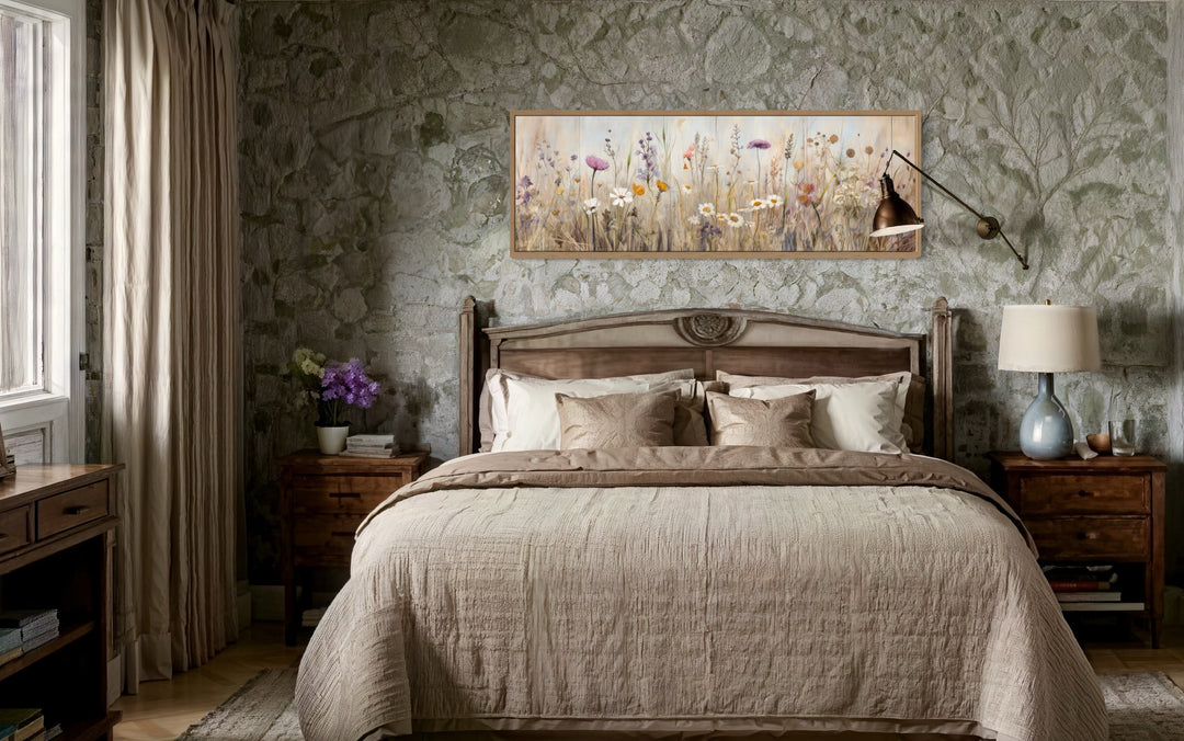 Horizontal framed canvas wall art of a neutral wildflower field above a bed in a rustic bedroom.