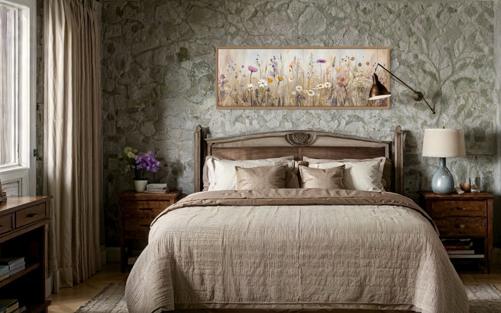 Horizontal framed canvas wall art of a neutral wildflower field above a bed in a rustic bedroom.