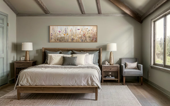 Horizontal framed canvas wall art of a neutral wildflower field above a wooden bed in a bedroom.