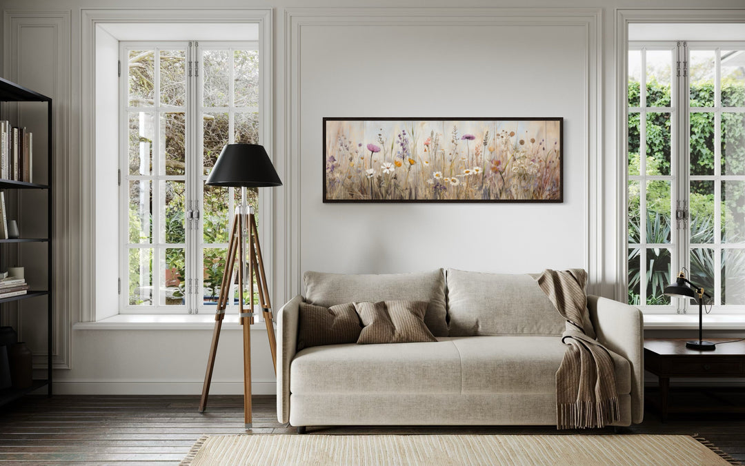 Horizontal framed canvas wall art of a neutral wildflower field above a beige sofa.