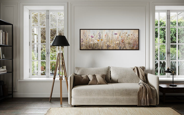 Horizontal framed canvas wall art of a neutral wildflower field above a beige sofa.