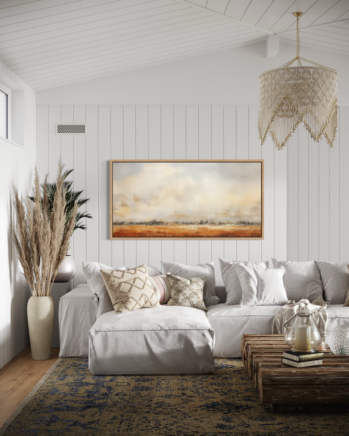 Minimalist farm field canvas art in a wooden frame above a white sofa in a rustic living room.