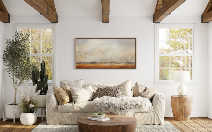 Minimalist farm field canvas painting in a wooden frame above a neutral sofa in a rustic living room