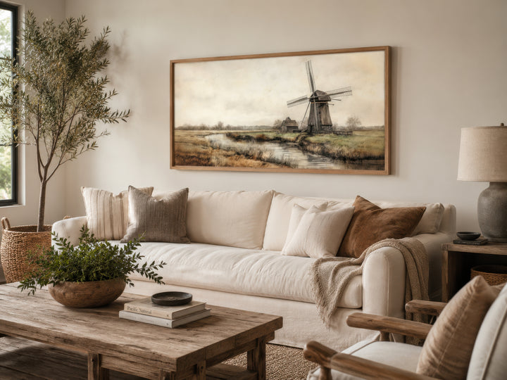 Vintage windmill canvas print in a wooden frame hanging above a white sofa in a rustic living room.